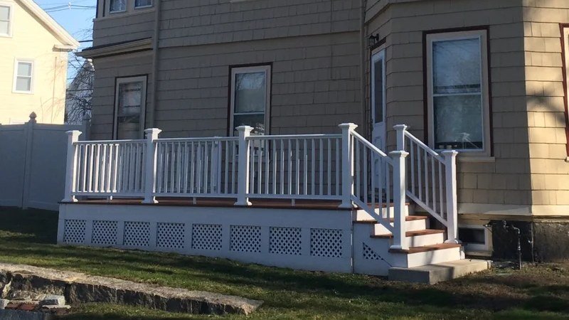 New deck with white railings, lattice skirting, and stairs on a tan-shingled home